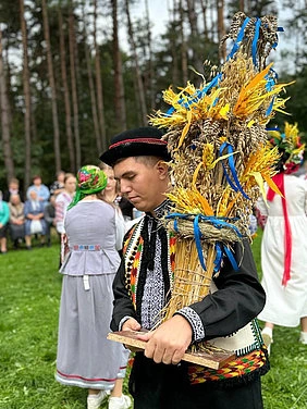 Чоловік у народному одязі тримає жнивець на святі врожаю.