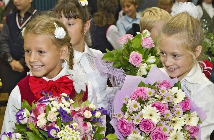 Дівчата в шкільних формах тримають квіти на урочистості.