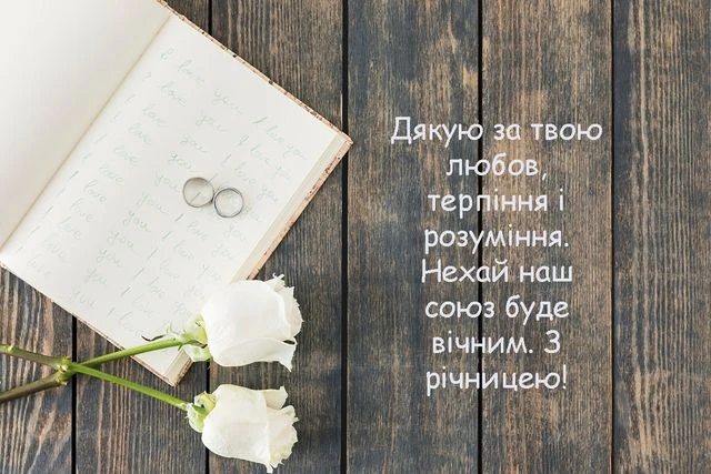 Білі троянди та кільця на дерев'яному фоні з привітанням українською.