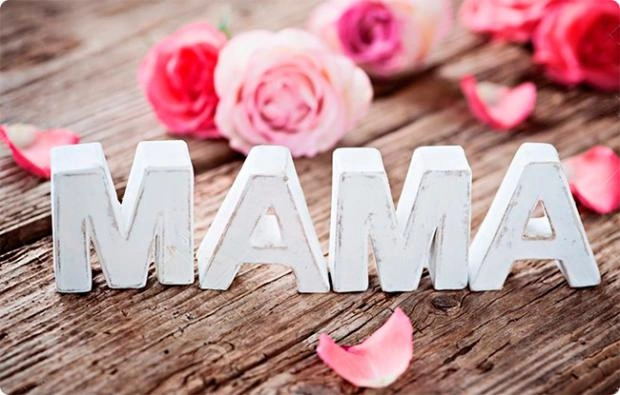 Білі літери МАМА на дереві з рожами та пелюстками.