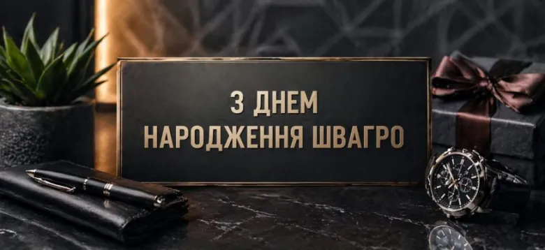 Чорна дошка з написом привітання та подарунками на столі.